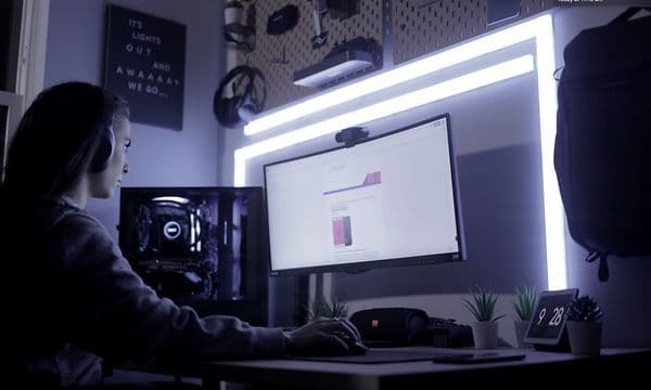 Kvinne med hodetelefoner sitter konsentrert foran PC med LIFX lysplankesett bak som lyser sterkt blåhvitt lys