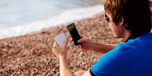 Man på strand som laddar sin smartphone med en powerbank