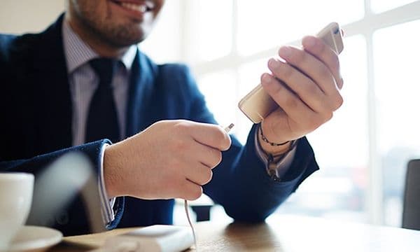 Glad man med kostym ansluter en powerbank i en smartphone