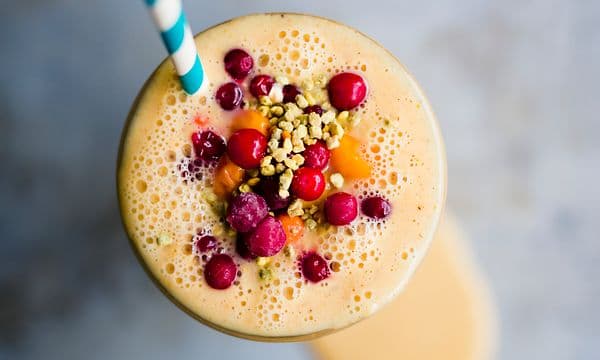 Oransje smoothie i glass med bær på toppen og sugerør