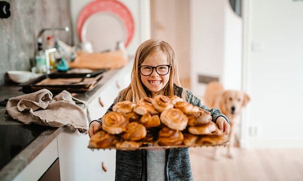 Jente som bærer et brett med kanelboller på et kjøkken