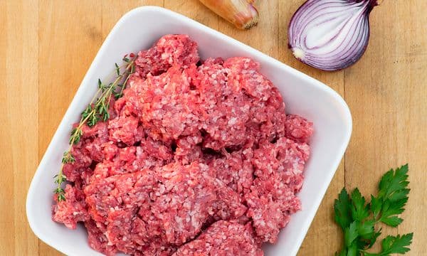 Malet kött i en vit skål på en köksbänk i trä, med lök och örter bredvid