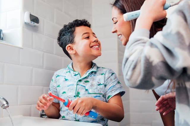Familie på badet og en liten gutt som viser tennene til moren sin og holder en elektrisk tannbørste i hånden