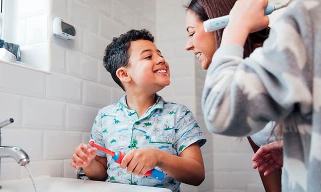 Familie på badet og en liten gutt som viser tennene til moren sin og holder en elektrisk tannbørste i hånden