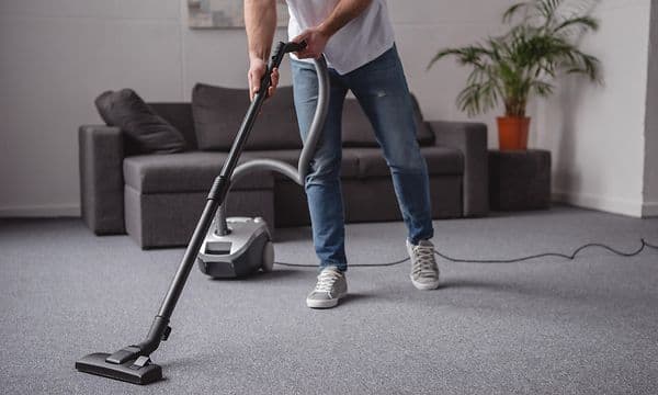 En mann støvsuger med en støvsuger med ledning i en grå stue