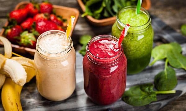 Tre glas med olika smoothies med grönsaker och frukt runt