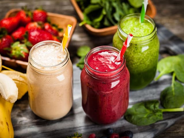 Tre glas med olika smoothies med grönsaker och frukt runt