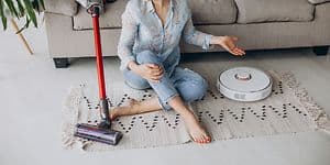 En kvinna sitter på golvet mellan en Dyson sladdlös dammsugare och en vit robotdammsugare