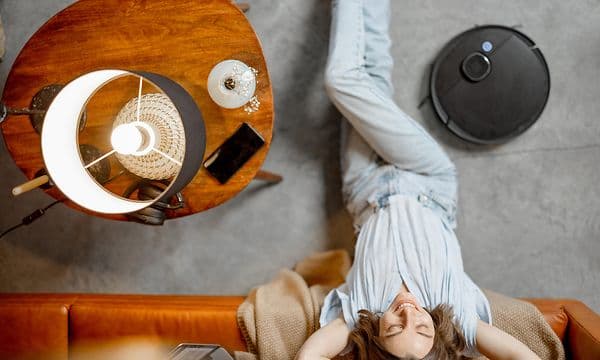Kvinna tar det lugnt vid en soffa medan en robotdammsugare dammsuger bredvid henne