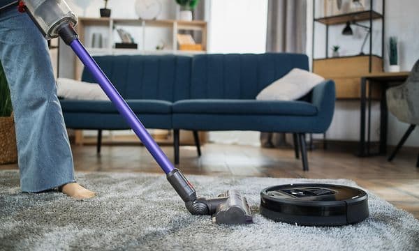 En person, der bruger en trådløs støvsuger i en stue ved siden af en sort robotstøvsuger