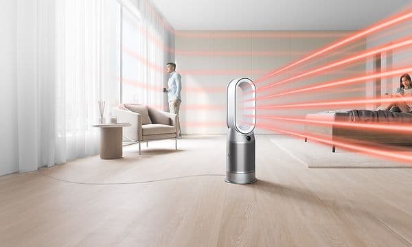 En Dyson luftrenser som sender ut varmestråler rundt i en stue og en mann som står i bakgrunnen