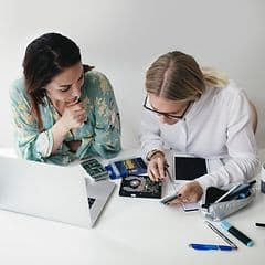 Kaksi naista korjaamassa elektroniikkalaitetta yhdessä