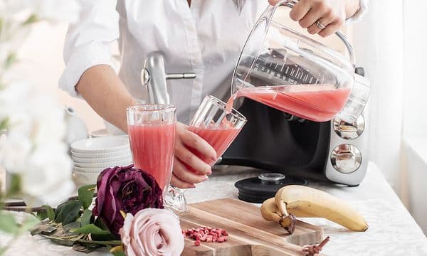 En kvinna i ett kök häller rosa juice från mixerkanna i ett glas