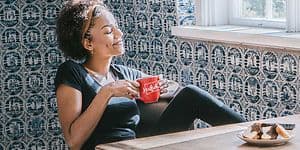 Kvinne som drikker fra kaffekopp med kaffemaskin på bordet