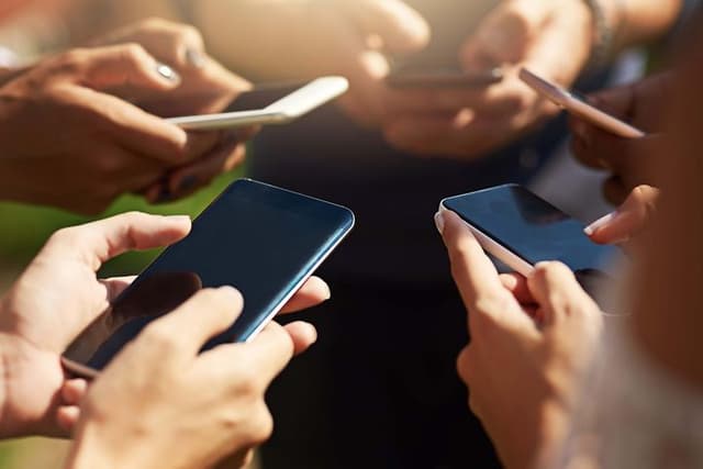 en gruppe personer står sammen og bruker smarttelefon utendørs