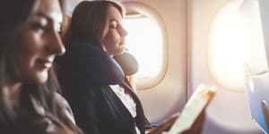 To kvinder slapper af i et fly, den ene med en nakkepude og den anden kigger på sin telefon