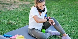 En kvinde tjekker sit smartwatch, mens hun sidder på en yogamåtte udendørs 