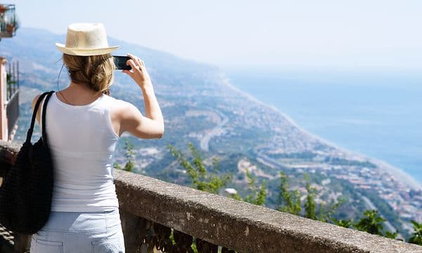 Fotografera med smartphone - Kvinna på semester använder sin smartphone för att ta en bild av en strand.