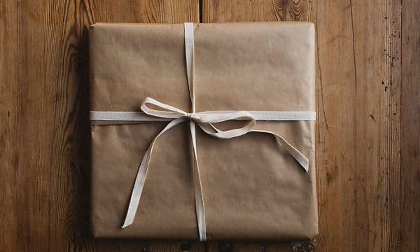 En gave pakket inn i brunt papir på et trebord