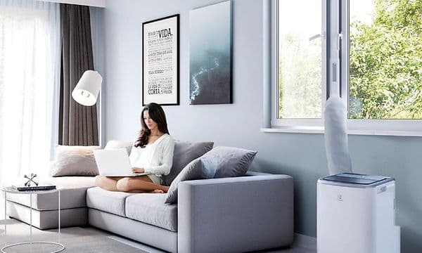 Kvinne jobber på sofaen med en bærbar aircondition ved siden av