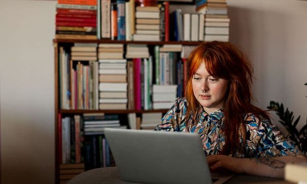 Kvinne som sitter ved macbook foran en bokhylle