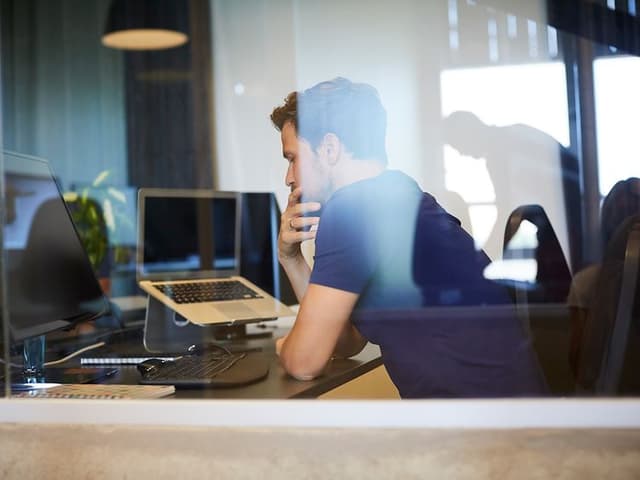 Mann som sitter ved pult og PC-utstyr og jobber