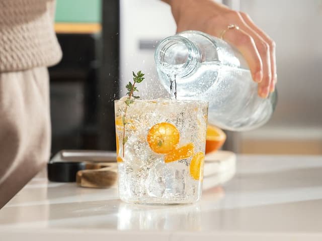 Person som häller kolsyrat vatten i ett glas