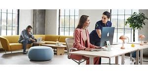 Två kvinnor bredvid en iMac och man som arbetar med MacBook
