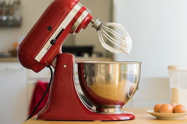 KitchenAid köksmaskin på ett bord, intill ägg och en plastbehållare med socker