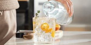 person heller boblefann fra en flaske over i et glass med frukt og isbiter