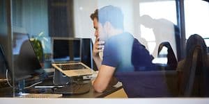 Man som sitter på ett kontor vid ett skrivbord med datorer framför sig och ser ut att fundera