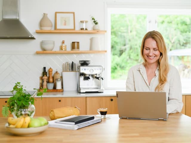 En kvinde sidder i sit køkken og arbejder på sin laptop
