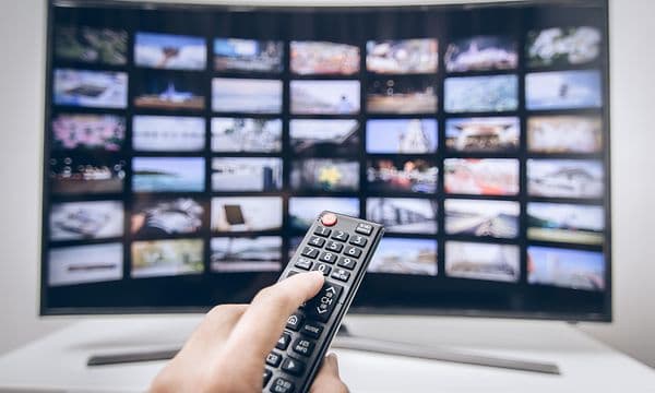 en tv med flere ulike apper åpen på skjerme og en hånd som holder fjernkontroll foran