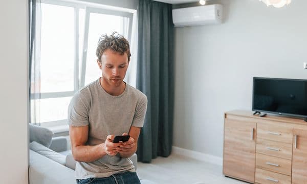 en ung mann justerer lysstyrken på en lampe via app på smarttelefon