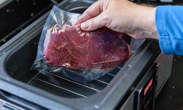 Person putter et kjøttstykke i vacuumert plast i en sous vide