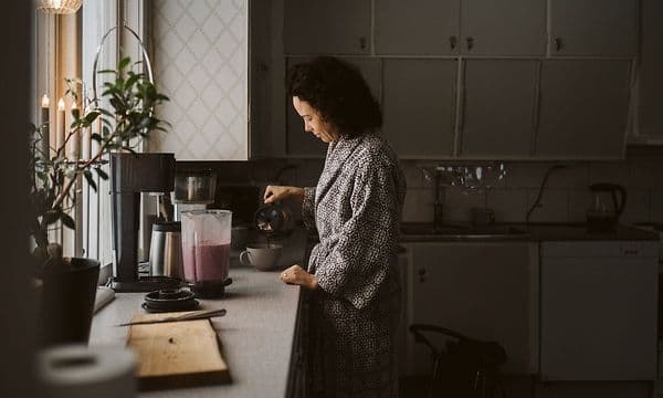 kvinne på et kjøkken med en blender på kjøkkenbenken