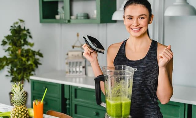en kvinne lager smoothie i en blender på kjøkken
