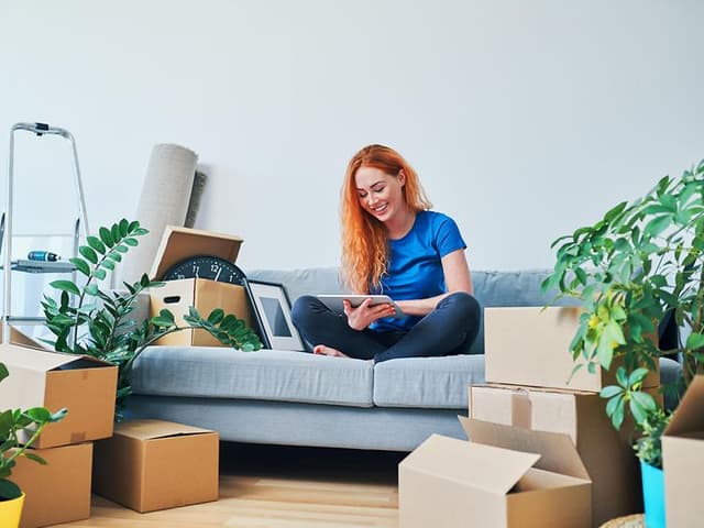 Nyindflyttet kvinde sidder i sofa med tablet