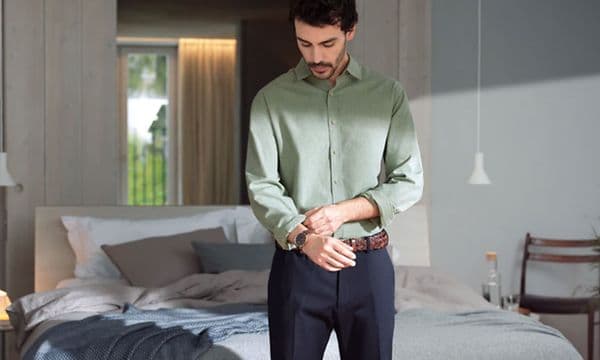 Man standing in front of a bed adjusting his sleeve on his shirt