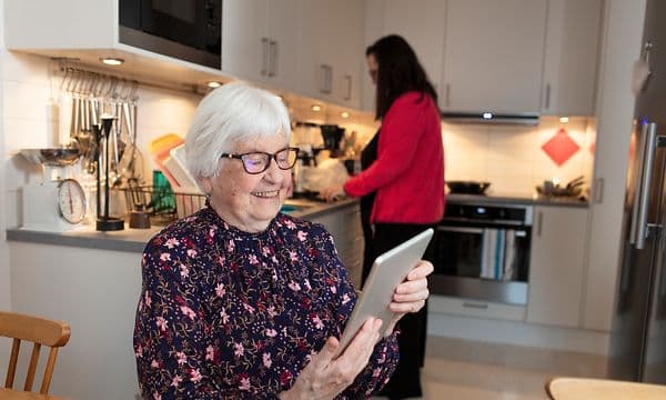 eldre kvinne bruker nettbrett på et kjøkken