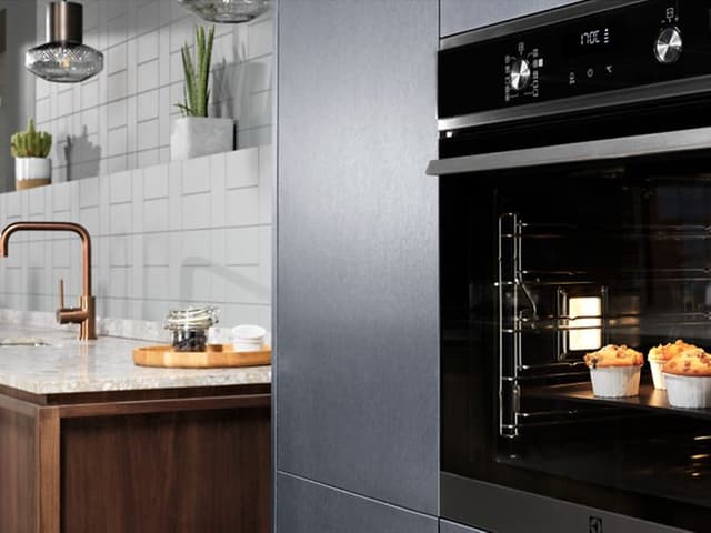 En dobbel Electrolux-ovn med muffins inni på et kjøkken og en vask i bakgrunnen