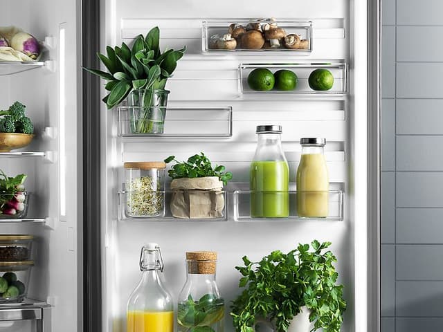 En åpen Electrolux kjøleskapsdør dekorert med smoothie, urter, lime, sopp, juice og vann