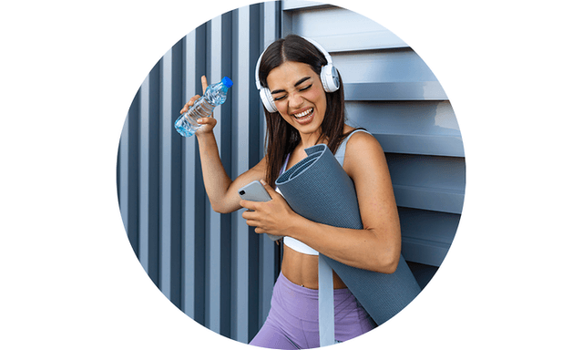 Grinning woman in yoga gear wearing headphones and holding smartphone