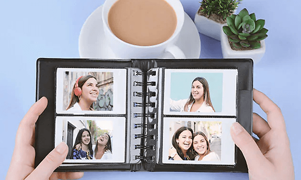 Person som holder fotoalbum med fire bilder over et blått bord med kaffe og plante på