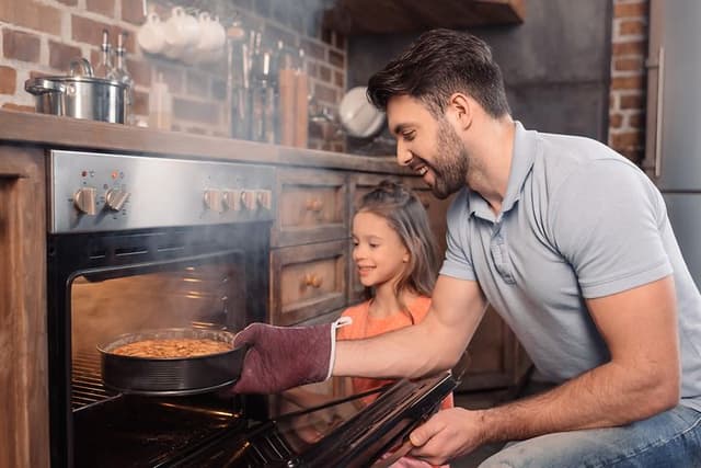 Father and daughter taking cake from oven