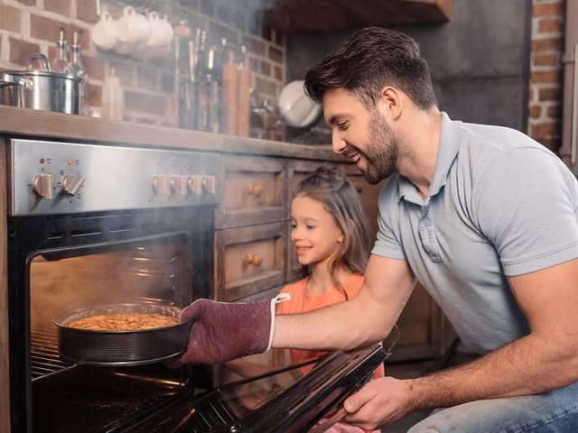 Father and daughter taking cake from oven
