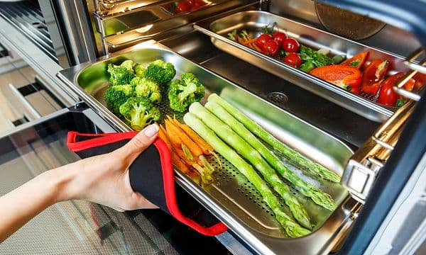Woman taking steamed vegetables out of steam oven