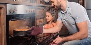 Far och dotter som ser glada ut tar ut en nybakad kaka från ugnen som ryker