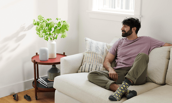 Man sittin in a white sofa while listening to something on his Google Nest Audio