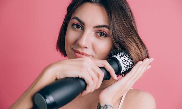 Kvinde på pink baggrund holder styler hår med varmluftbørste
